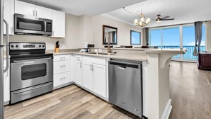 A modern kitchen with stainless steel appliances, white cabinetry, and a view of the ocean. - Majestic Beach Towers 1-2003 (Panama City Beach)