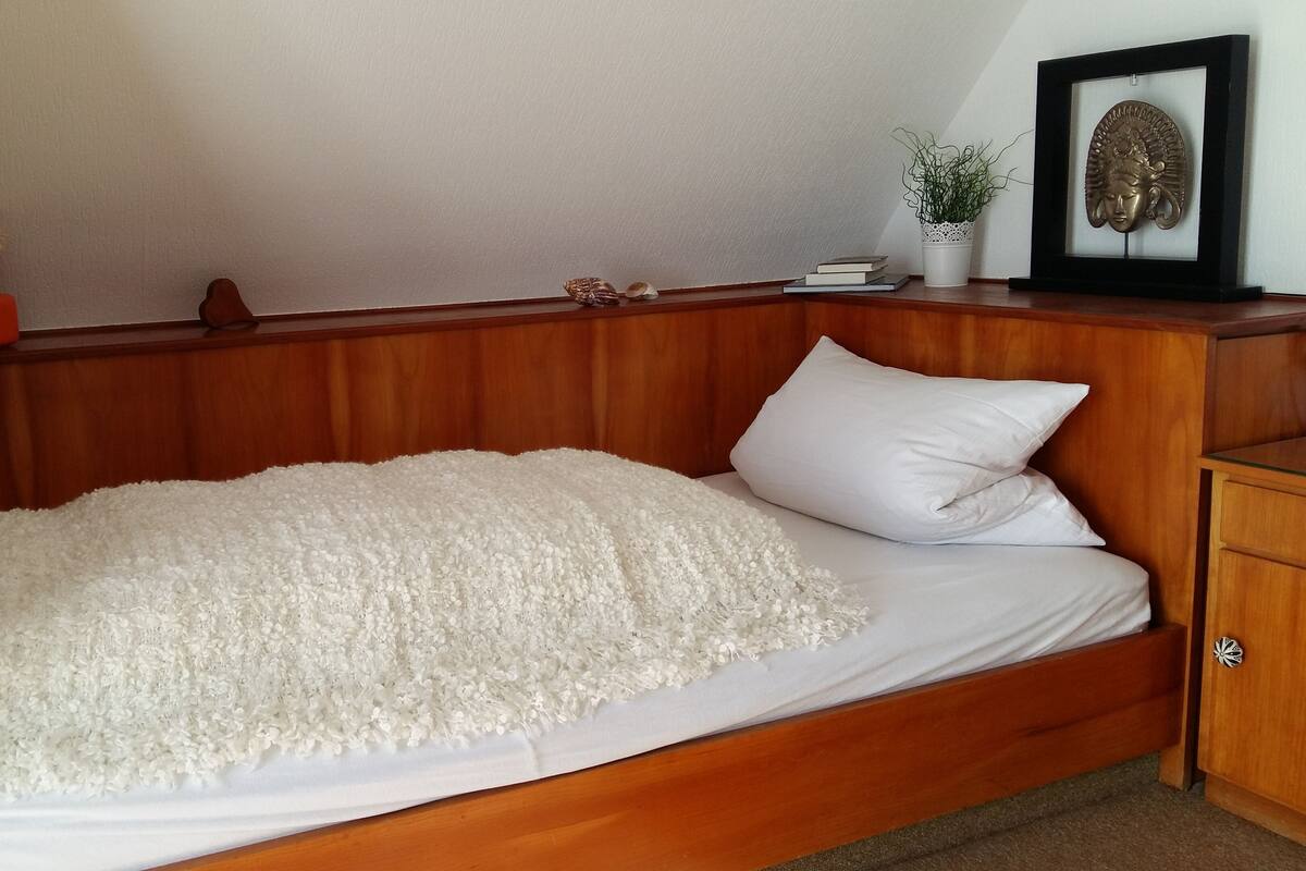 Un lit en bois avec une couvre-lit à motifs floraux blancs et un oreiller blanc.