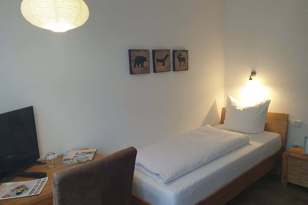 Une chambre d’hôtel bien rangée, avec un lit, un bureau équipé d’un ordinateur, une chaise et une lampe. Trois tableaux représentant des animaux sont accrochés aux murs.