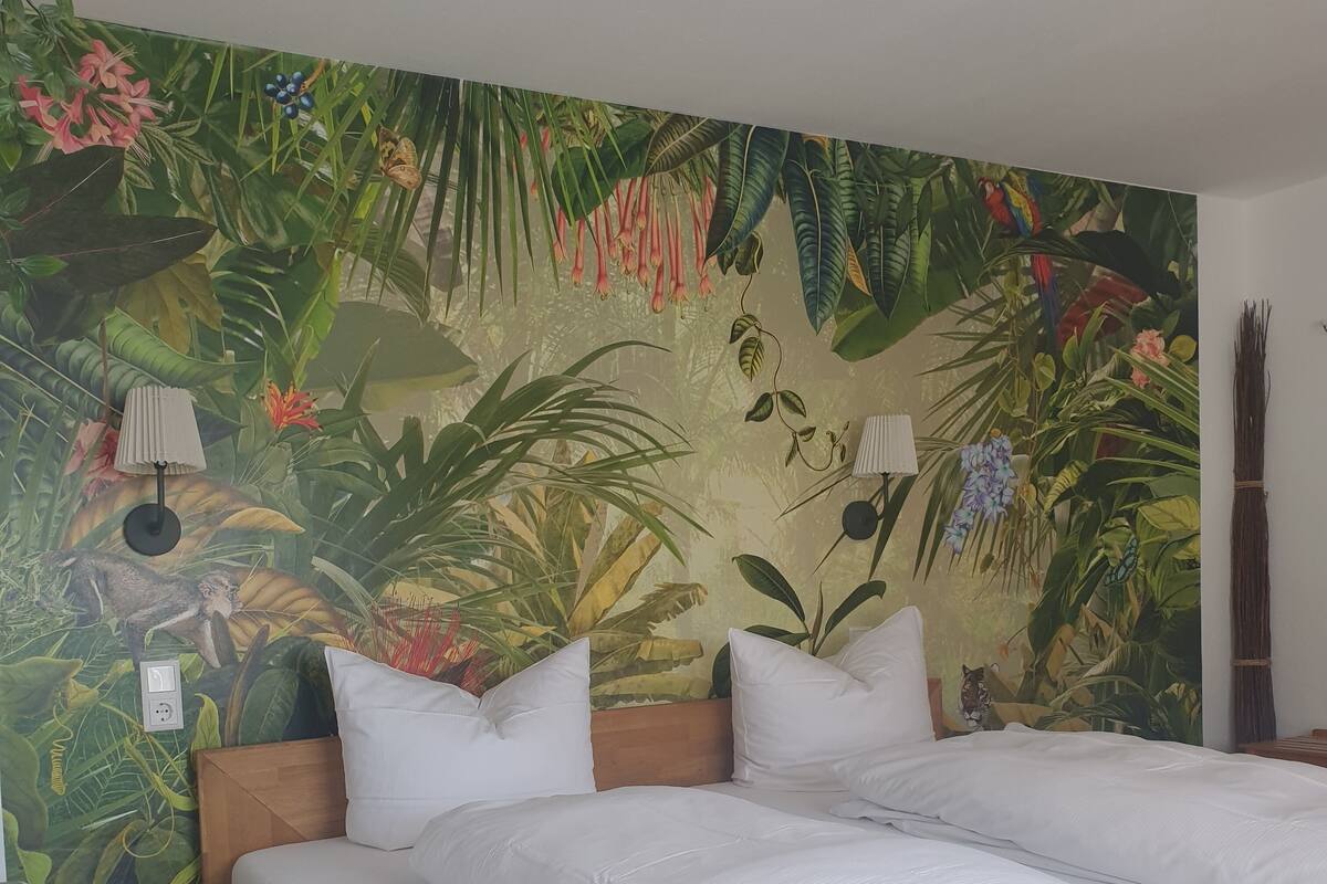 Une chambre à coucher comprenant un lit, deux tables de chevet, une lampe et une fresque murale sur le thème des tropiques.