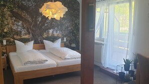 Un dormitorio con cama, lámpara colgante, ventana con cortinas y un mural en la pared.