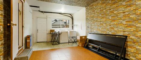Una habitación amplia con piso de madera, un banco, una zona de cocina con ventanal y pared de piedra.