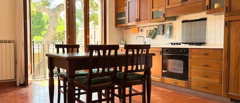 A kitchen with wooden cabinets, a dining table with chairs, and a view through large windows.