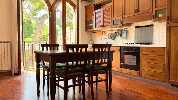 A kitchen with wooden cabinets, a dining table with chairs, and a view through large windows. - P074 – Porto Recanati, apartment with garage, 50 meters from the sea (Porto Recanati)