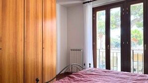 A bedroom with a bed, wooden wardrobe, and a window with a view of greenery. - P074 – Porto Recanati, apartment with garage, 50 meters from the sea (Porto Recanati)