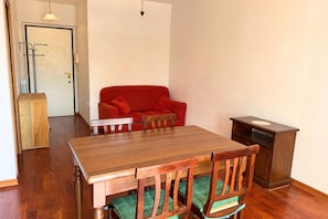 A dining area with a wooden table, green cushioned chairs, a red sofa, and a small cabinet.