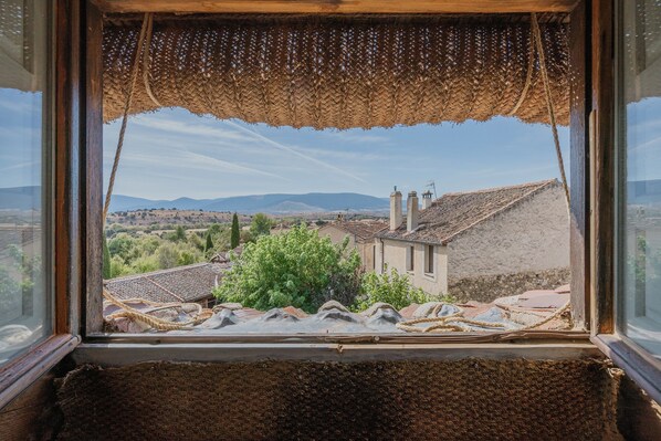 A window with a woven blind, a view of buildings, and a distant landscape. - Holiday Home 'La Casa Del Herrero' with Mountain View, Private Garden and Wi-Fi (Requijada)
