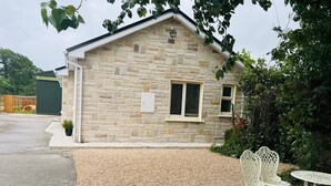 A stone building with a sloped roof, a small window, and a door. There is a gravel area in front with a white metal table and chairs. - Charming 2-bedroom cottage nea Maynooth University with WiFi (Maynooth)