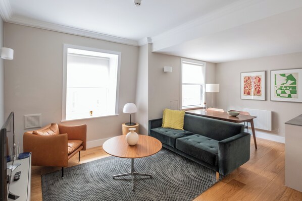 Un salon moderne avec un fauteuil en cuir, un canapé vert, une table basse ronde en bois et un tapis gris.