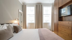 A hotel room with a bed, a TV, and a wooden dresser. - Native Bank (London)