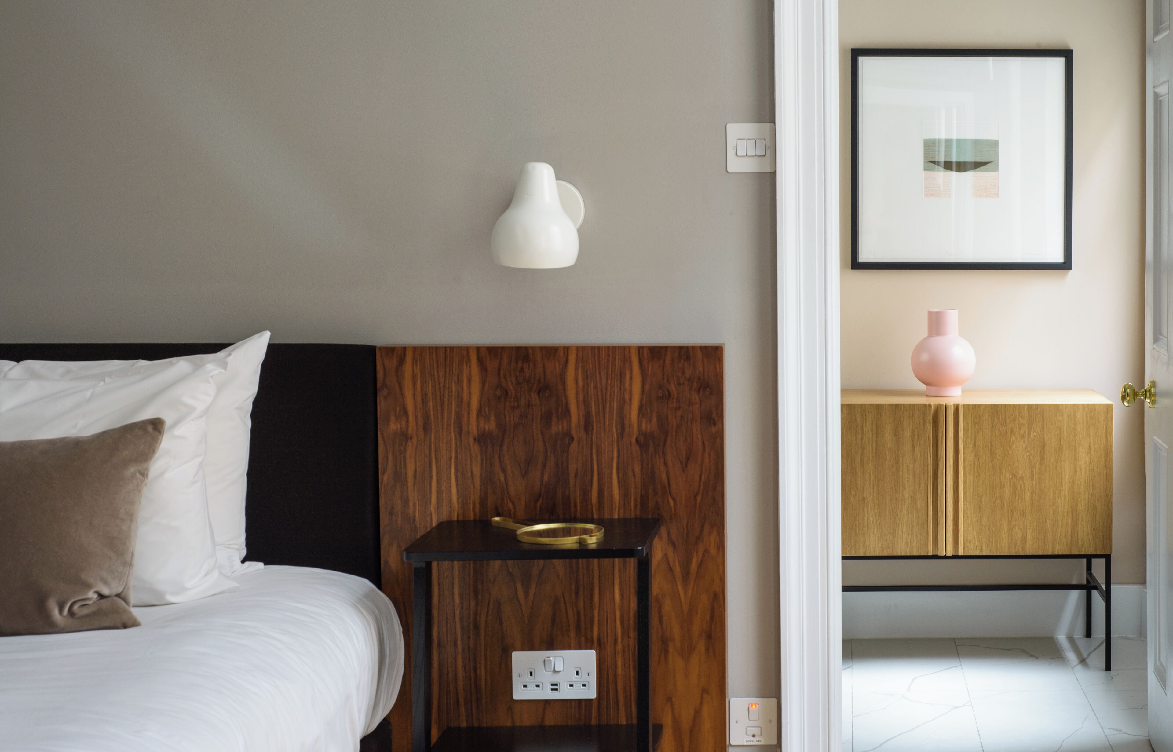 Une chambre à coucher comprenant un lit, une table de chevet, une lampe fixée au mur et un tableau encadré.