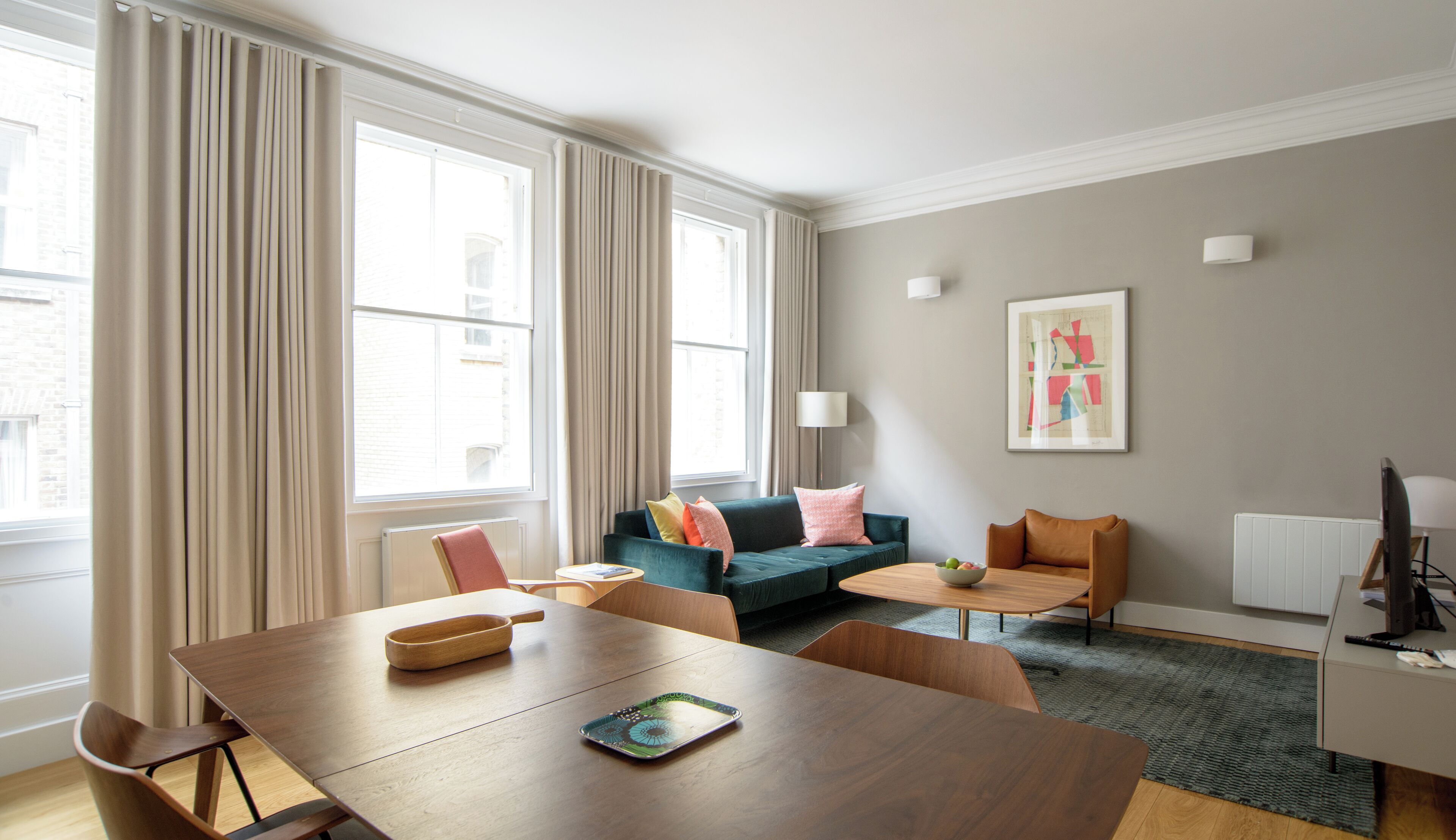 Una sala de estar moderna con una mesa de comedor de madera, un sofá con cojines de colores, una pequeña mesa de centro y una lámpara.