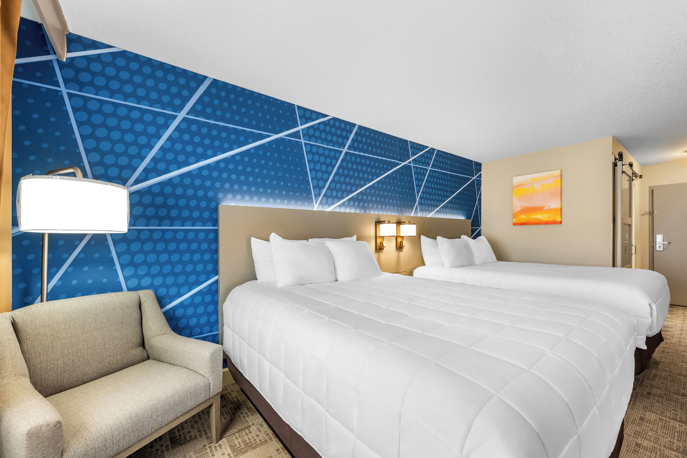 Habitación de hotel con una cama grande, un sofá, una pared con estampado geométrico y un cuadro.