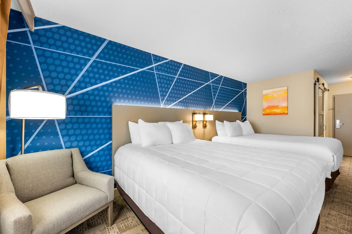 A hotel room with a large bed, a chair, a wall with a geometric pattern, and a painting.