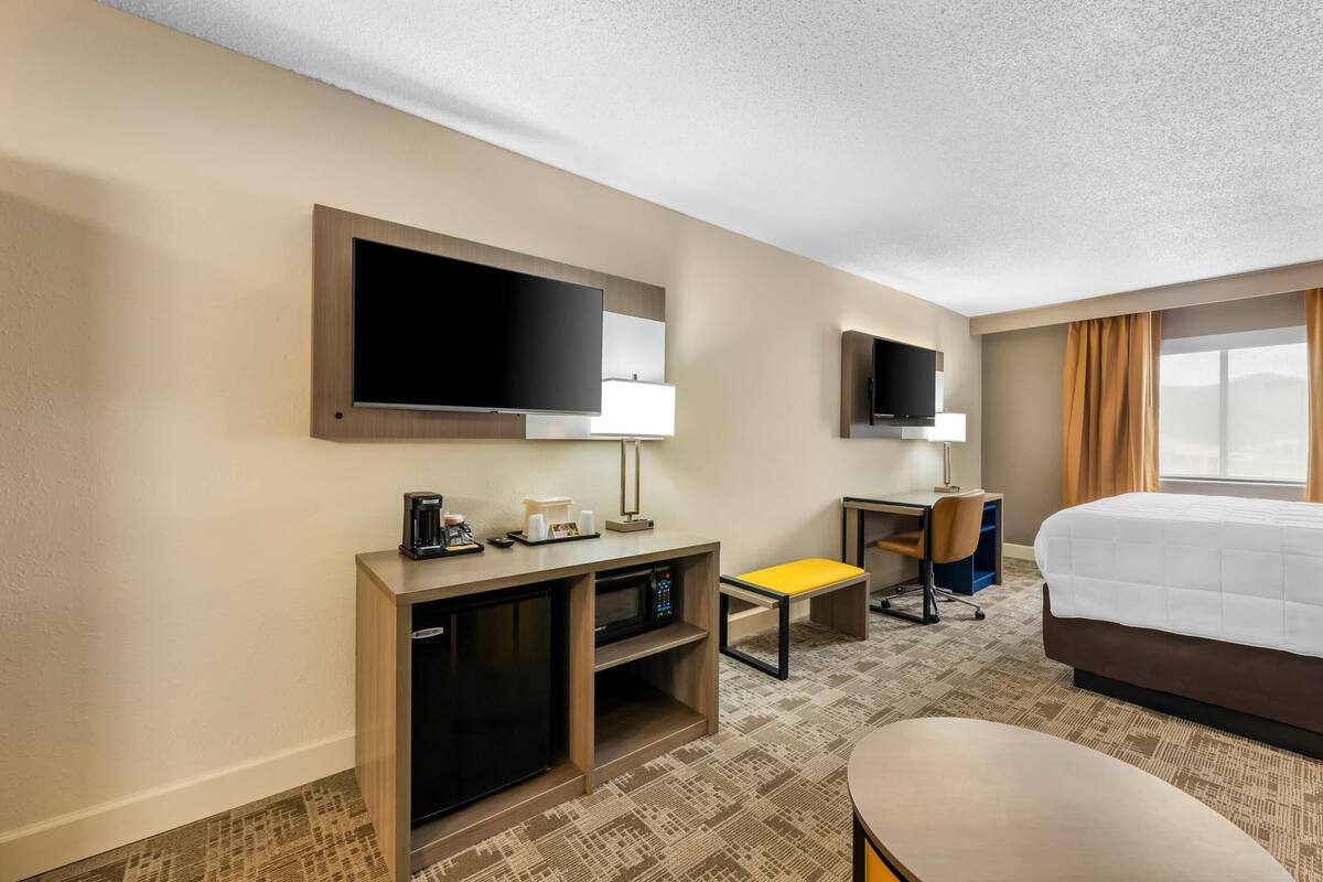 A hotel room with a bed, a desk, a television, a microwave, and a seating area.