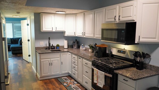 A modern kitchen with white cabinets, granite countertops, stainless steel appliances, and a visible microwave.