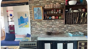 A kitchen with a stove, oven, and a shelf with jars and kitchen utensils.