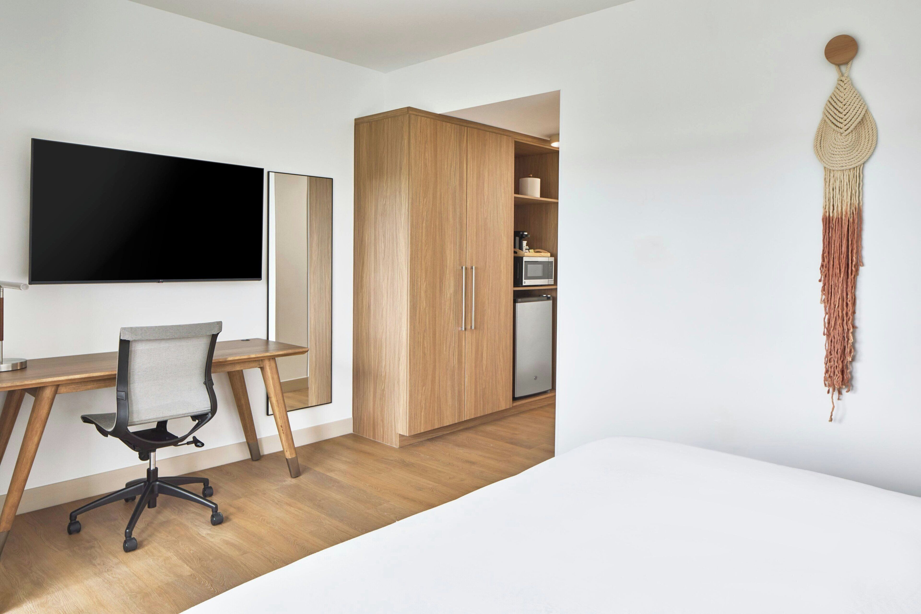 Ein modernes Zimmer mit Schreibtisch aus Holz, einem Flachbildfernseher und einer Küchenzeile.