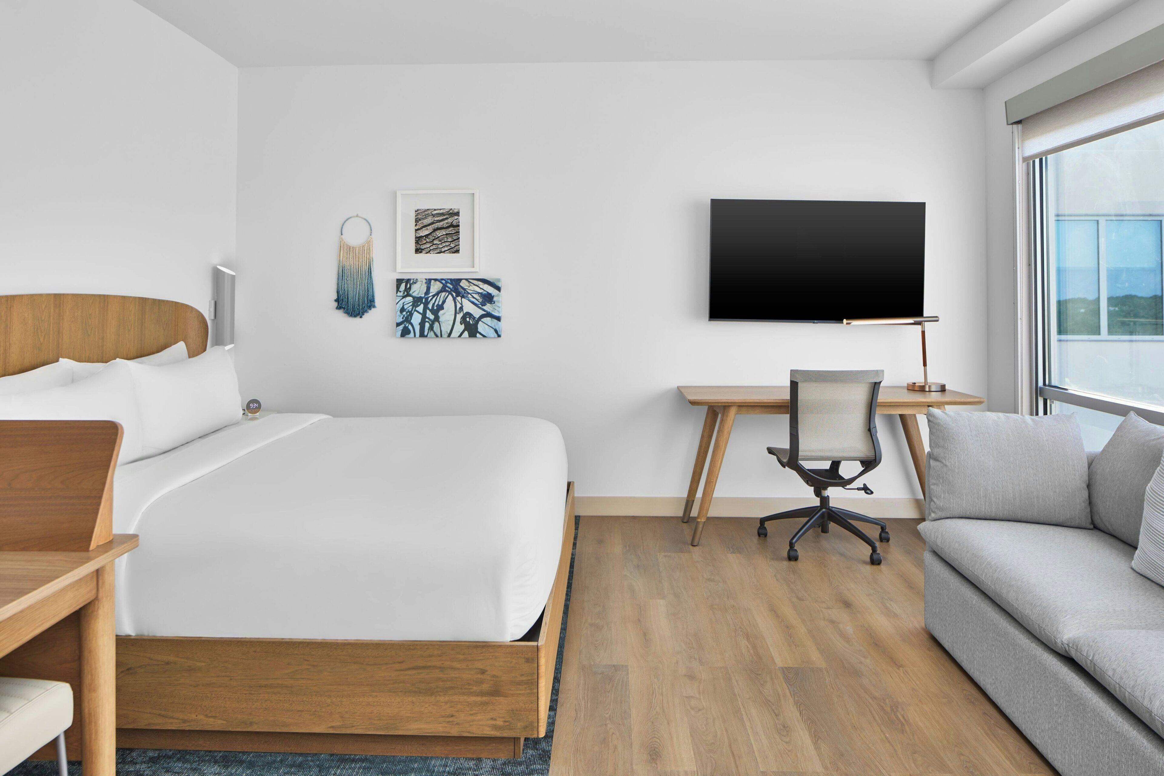 A modern hotel room with a large bed, a desk, a chair, and a sofa.