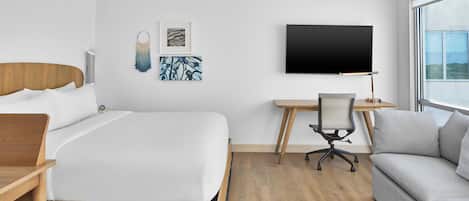 A modern hotel room with a large bed, a desk, a chair, and a sofa.