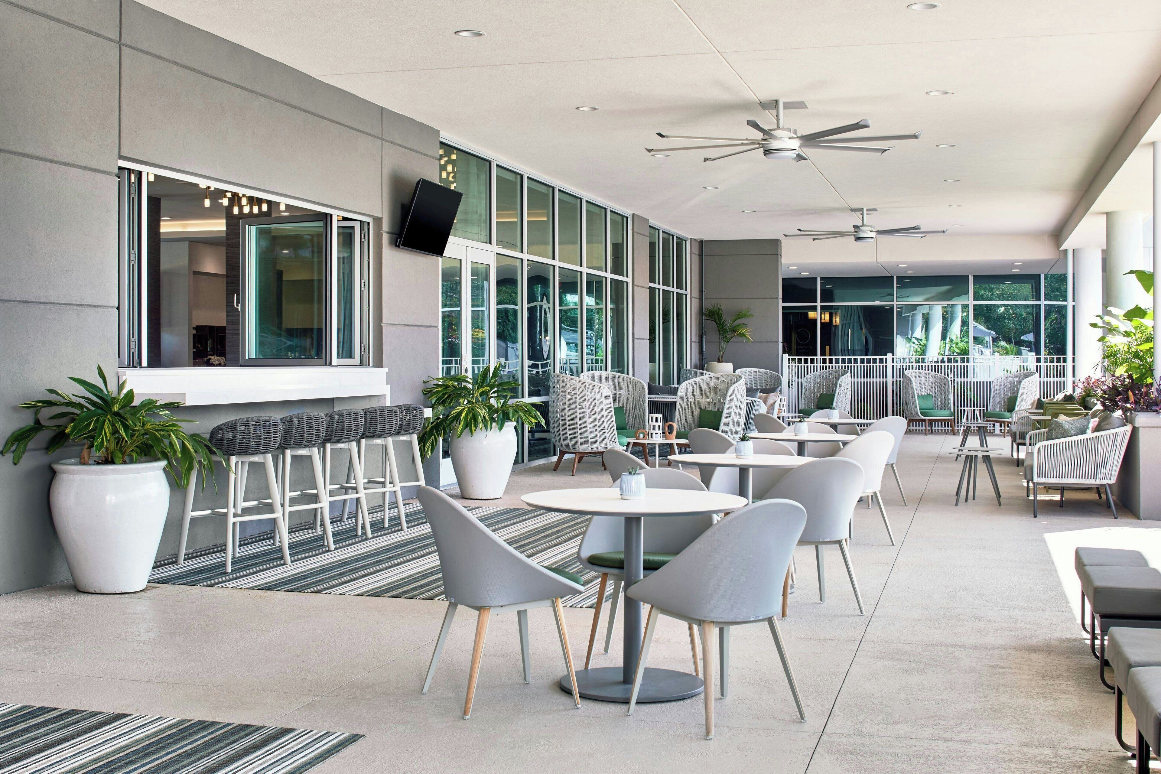 A modern outdoor seating area with white and grey chairs, tables, and potted plants.