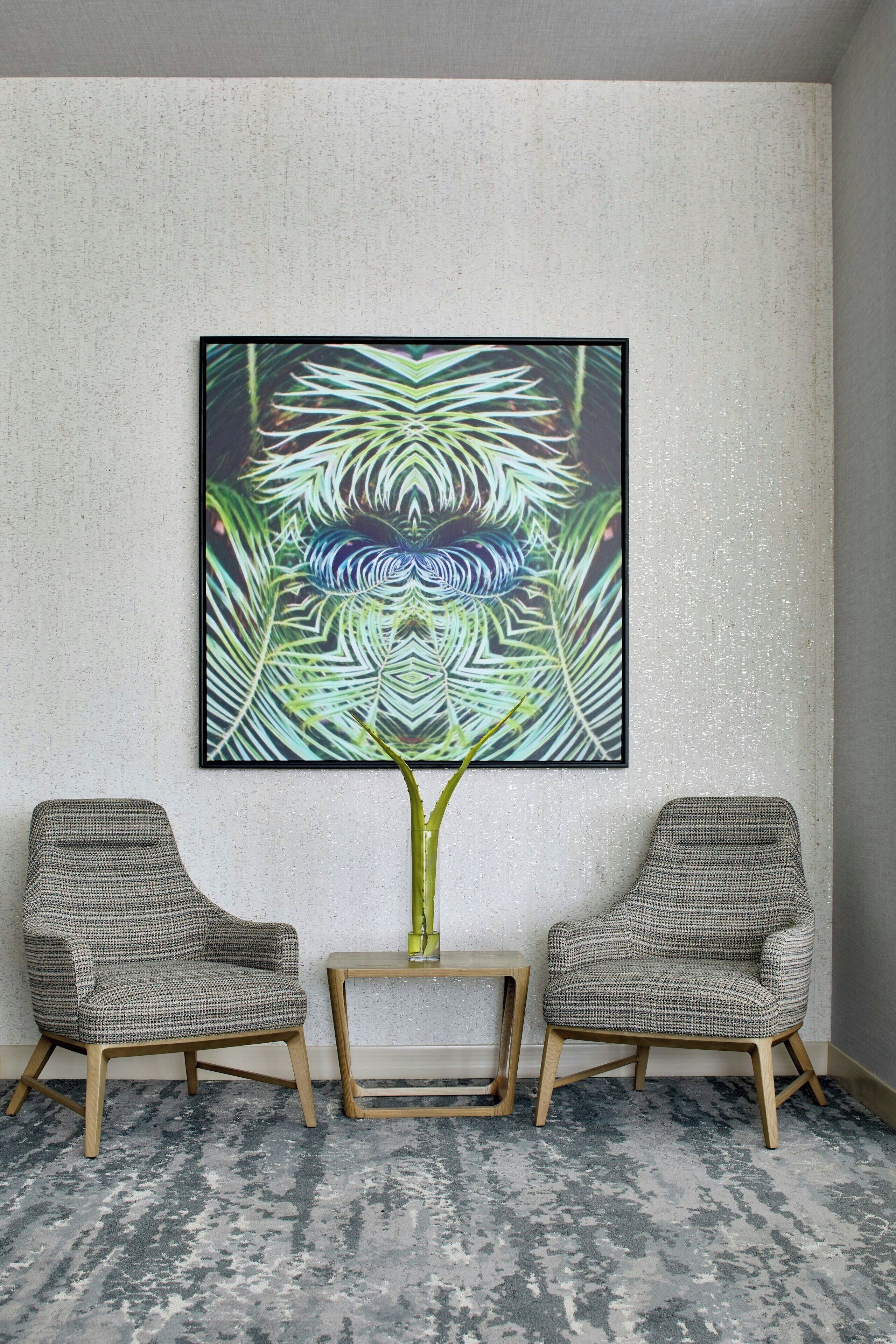 Una habitación con un cuadro abstracto grande en la pared, dos sillas estampadas y una pequeña mesa de madera.
