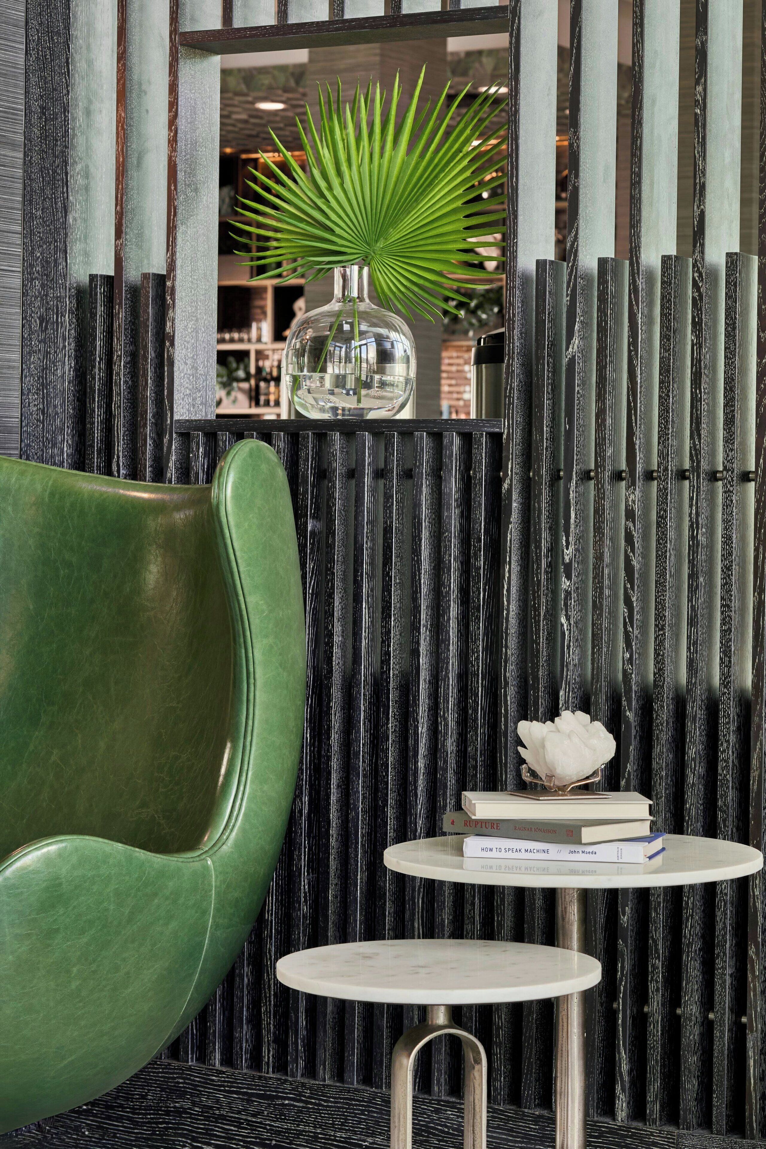 A modern interior with a green chair, a small table with books, and a decorative vase with a plant.