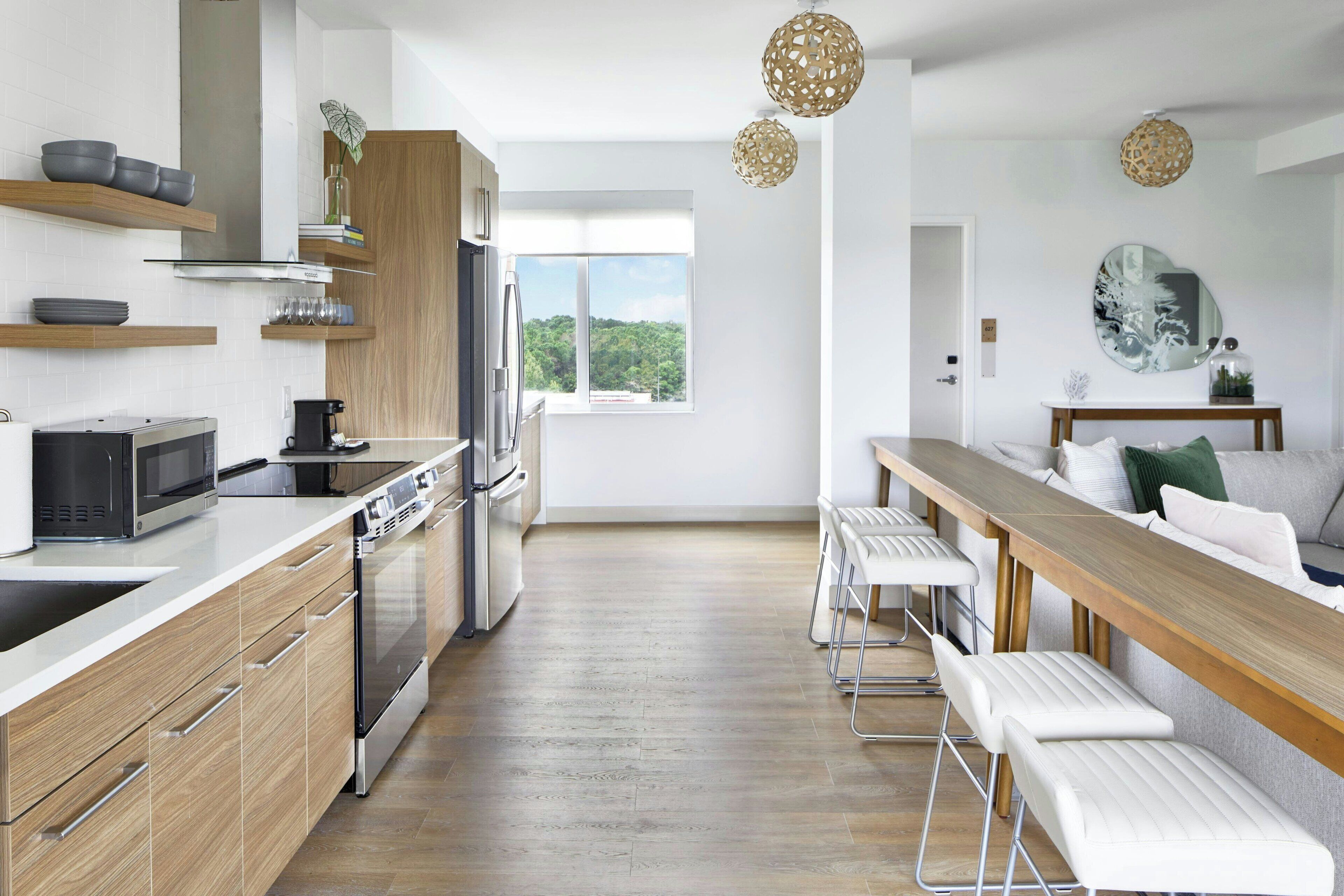 A modern kitchen with wooden cabinets, stainless steel appliances, and a long dining table with white bar stools.