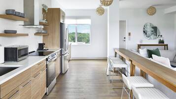 A modern kitchen with wooden cabinets, stainless steel appliances, and a long dining table with white bar stools.