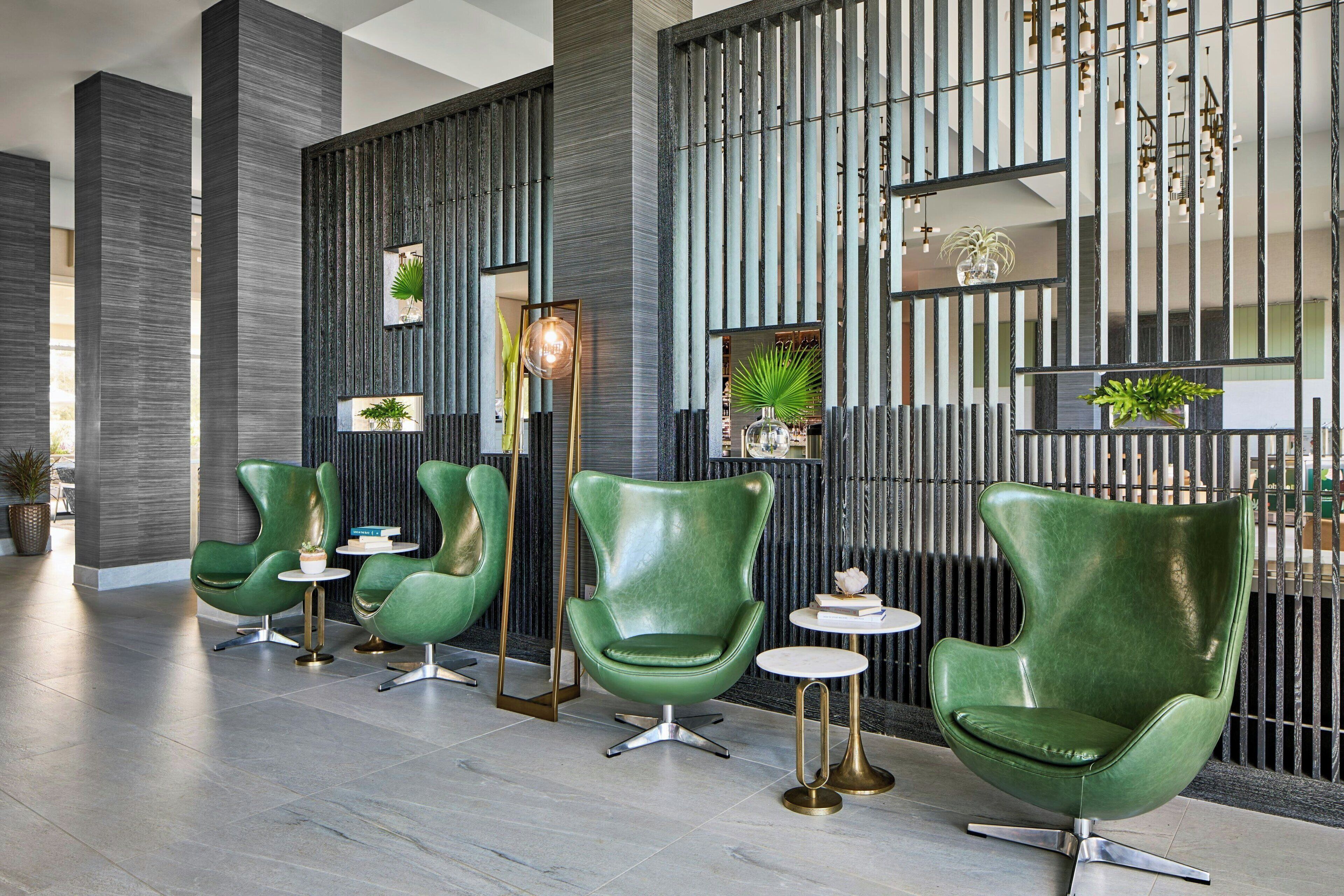 A modern lobby with green leather chairs, a tall column, and a decorative wall with vertical lines and plants.
