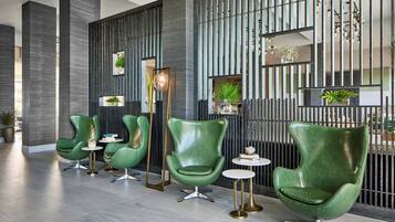A modern lobby with green leather chairs, a tall column, and a decorative wall with vertical lines and plants.