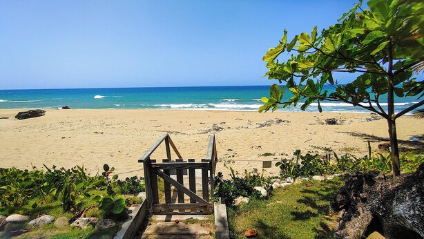 A wooden staircase leading to a sandy beach with the ocean in the background. - 2-bedroom condo in serene Perla Marina with AC, WiFi. Enjoy relaxation (Playa Perla Marina)