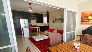 A modern living space with a kitchen, a dining area with a grill, and a sofa with red cushions. - 2-bedroom condo in serene Perla Marina with AC, WiFi. Enjoy relaxation (Playa Perla Marina)