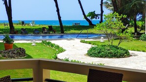 A pool area with lounge chairs and a view of the ocean. - 2-bedroom condo in serene Perla Marina with AC, WiFi. Enjoy relaxation (Playa Perla Marina)