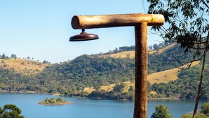 A wooden structure with a hanging object, surrounded by a lake and hilly landscape. - Nest Altar (Joanópolis)