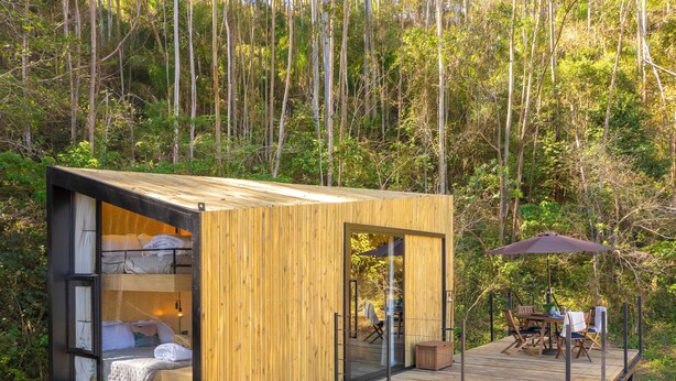 A wooden cabin with a glass-enclosed bedroom, a deck with outdoor seating, and a forest backdrop. - Nest Altar (Joan ópolis)