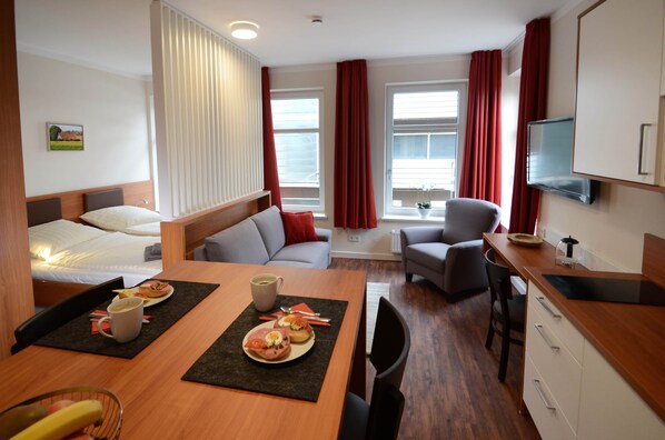 A hotel room with a bed, a dining table with breakfast, a sofa, a TV, and a desk. - Zum Brandenburger Tor 05 (Unknown)