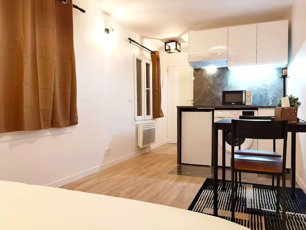 A compact kitchen with a microwave, a small refrigerator, and a dining area with a table and chair.