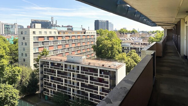 Un immeuble de grande hauteur, doté de nombreux étages et de balcons, entouré d’autres immeubles et d’arbres.