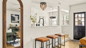 A modern kitchen with a white countertop, bar stools, and a hanging light fixture.