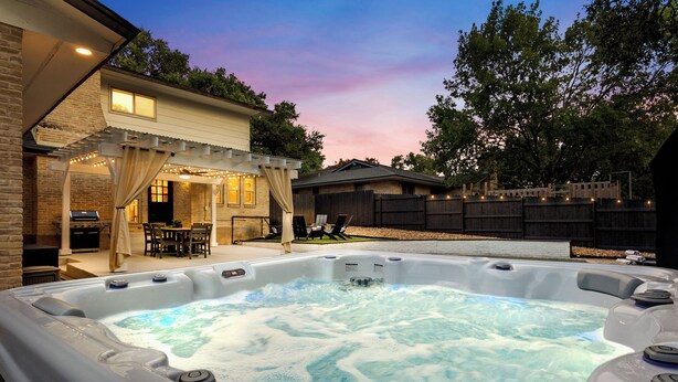 A hot tub in a backyard with a covered patio and a wooden fence.