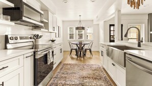 A modern kitchen with white cabinetry, a stainless steel stove, and a dining area with a patterned rug.