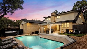 A backyard with a swimming pool, lounge chairs, and a covered patio area.