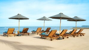 A beach with wooden lounge chairs and umbrellas. - Hilton Garden Inn Bali Nusa Dua (Nusa Dua)