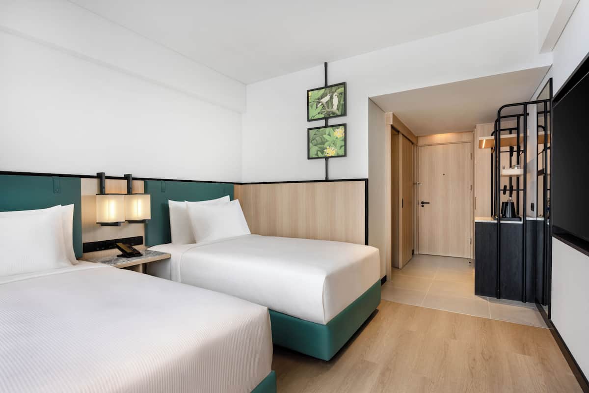 Ein Hotelzimmer mit zwei Betten, einem Schreibtisch mit Lampe, einem Kleiderschrank und einer Küchenzeile.