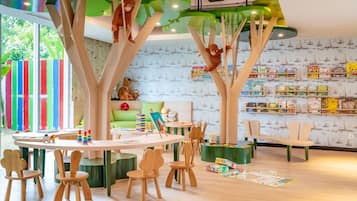 Uma área de recreação infantil com mobiliário de madeira, parede verde com estantes e cerca colorida listrada.