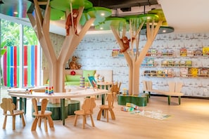 Ein Kinderspielbereich mit Holzmöbeln, einer grünen Wand mit Bücherregalen und einem farbenfrohen, gestreiften Zaun.