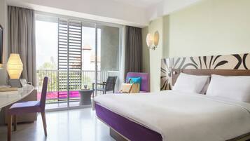 Quarto de hotel com cama, escrivaninha, cadeira, varanda e vista, além de parede com cabeceira decorativa.