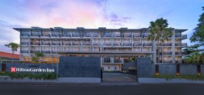 A multi-story hotel with balconies, a gated entrance, and a landscaped area. - Hilton Garden Inn Bali Nusa Dua (Nusa Dua)