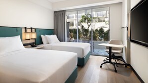 Une chambre d’hôtel avec deux lits, un bureau, une chaise, une télévision et un balcon donnant sur l’extérieur.